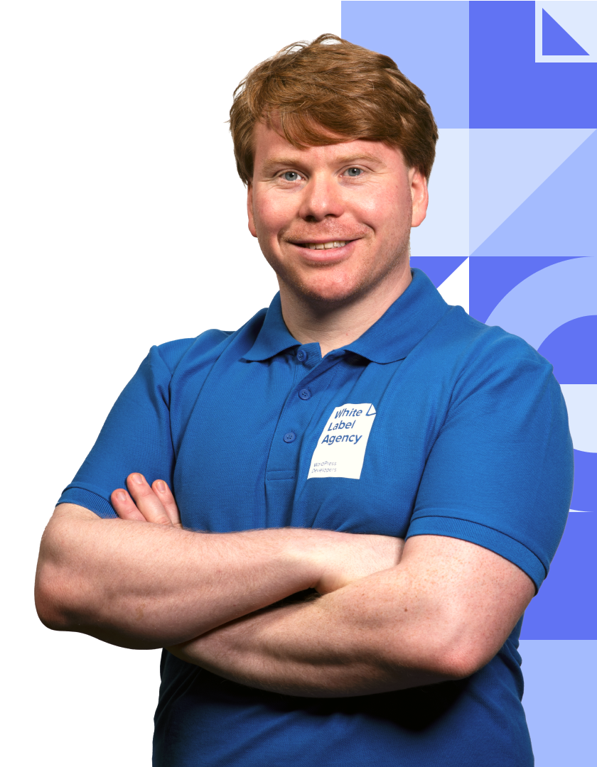 A smiling man with reddish-brown hair, wearing a blue polo shirt with a "White Label Agency" logo. He is posing with his arms crossed