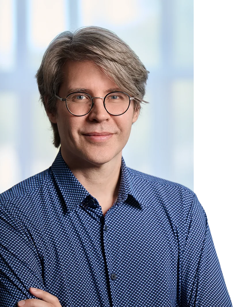 Portrait of a smiling man with salt-and-pepper hair and round glasses wearing a blue patterned shirt.