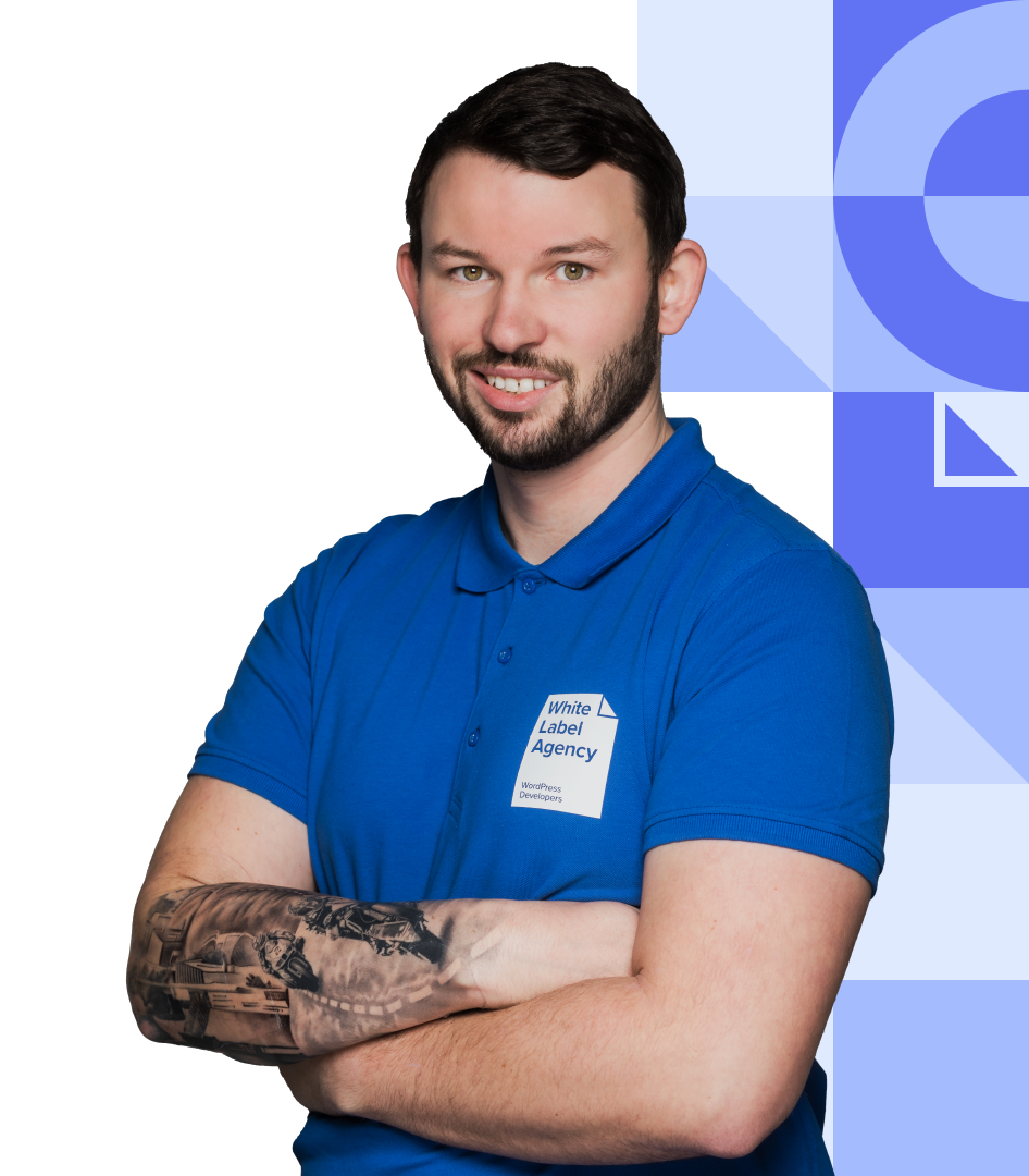 A portrait of a smiling man with a beard and a forearm tattoo, wearing a bright blue polo shirt with a "White Label Agency" logo, posing with arms crossed.