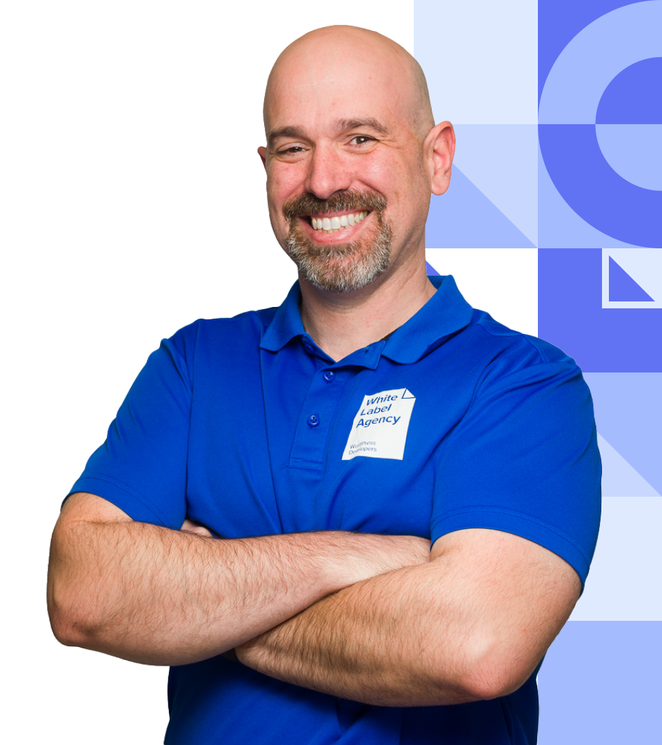 A smiling, bald man with a grey goatee, wearing a bright blue polo shirt with a "White Label Agency" logo, posing with arms crossed.